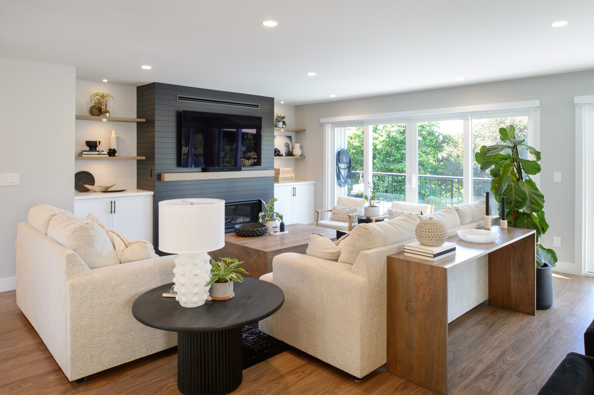 Corner shot of the living room with tv and fireplace against black shiplap background, surrounded by light beige walls. Lit up with natural lighting through the sliding doors to the right of the room.