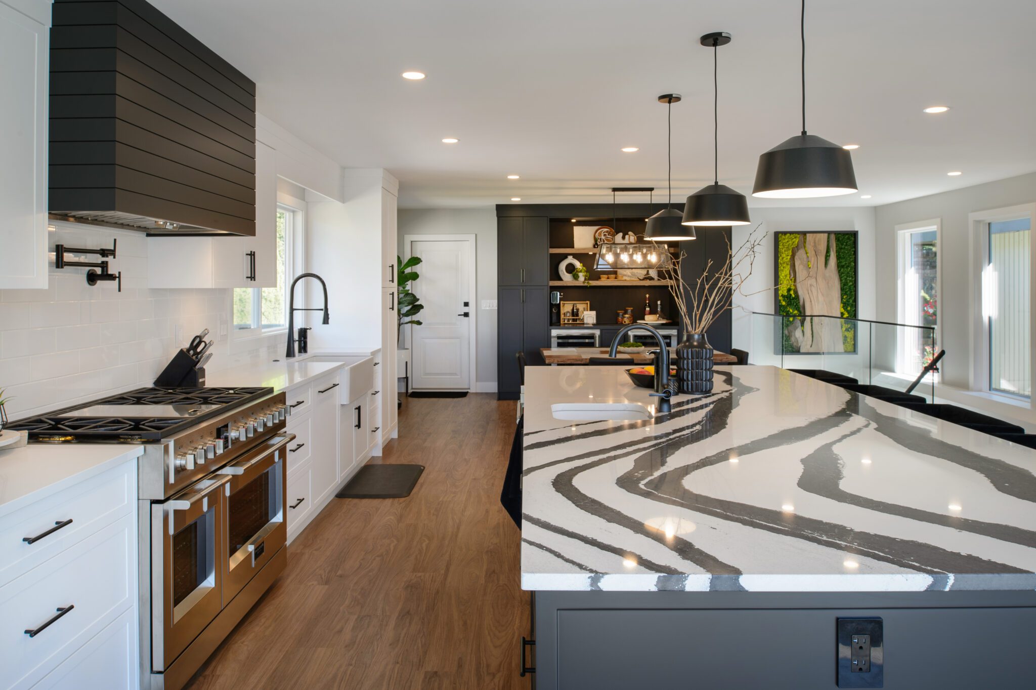 Lengthwise view of the kitchen, with black and white marbled quartz island to the right, and range and sink to the left.