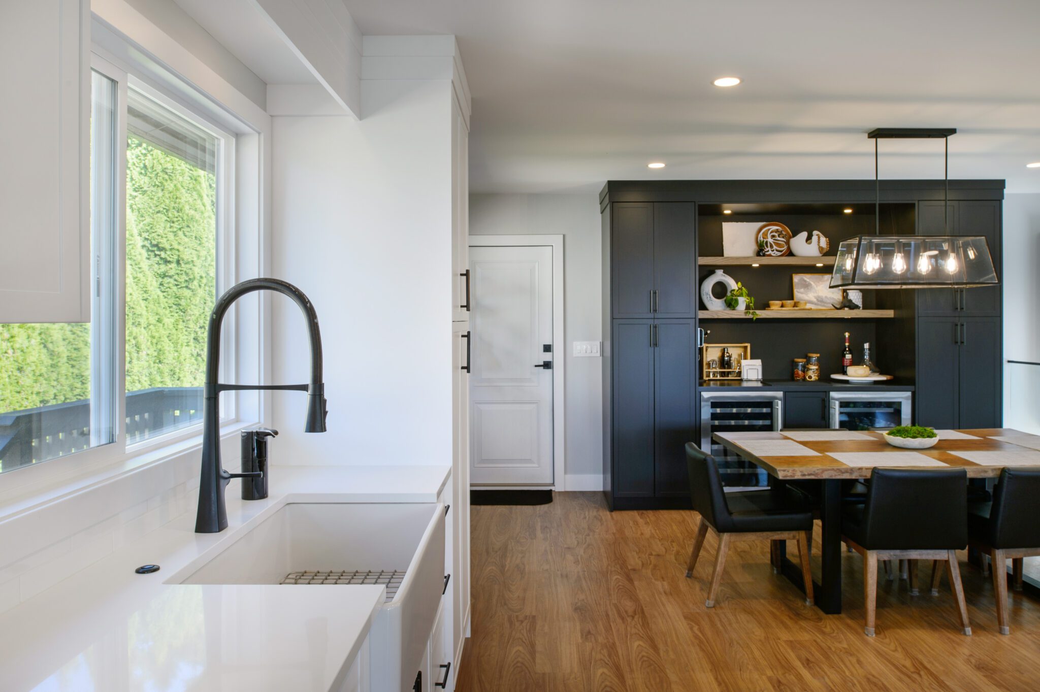 White farmhouse sink with black faucet sits in front of a window, with a black cabinet in the background.