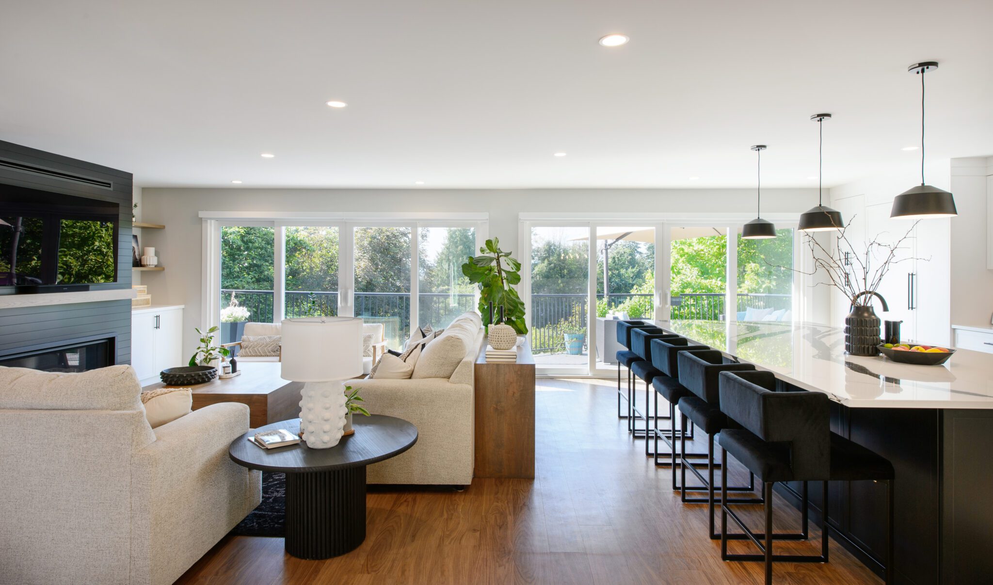 Linear view of living room couches across from island seating with wall-to-wall sliding glass doors in background.