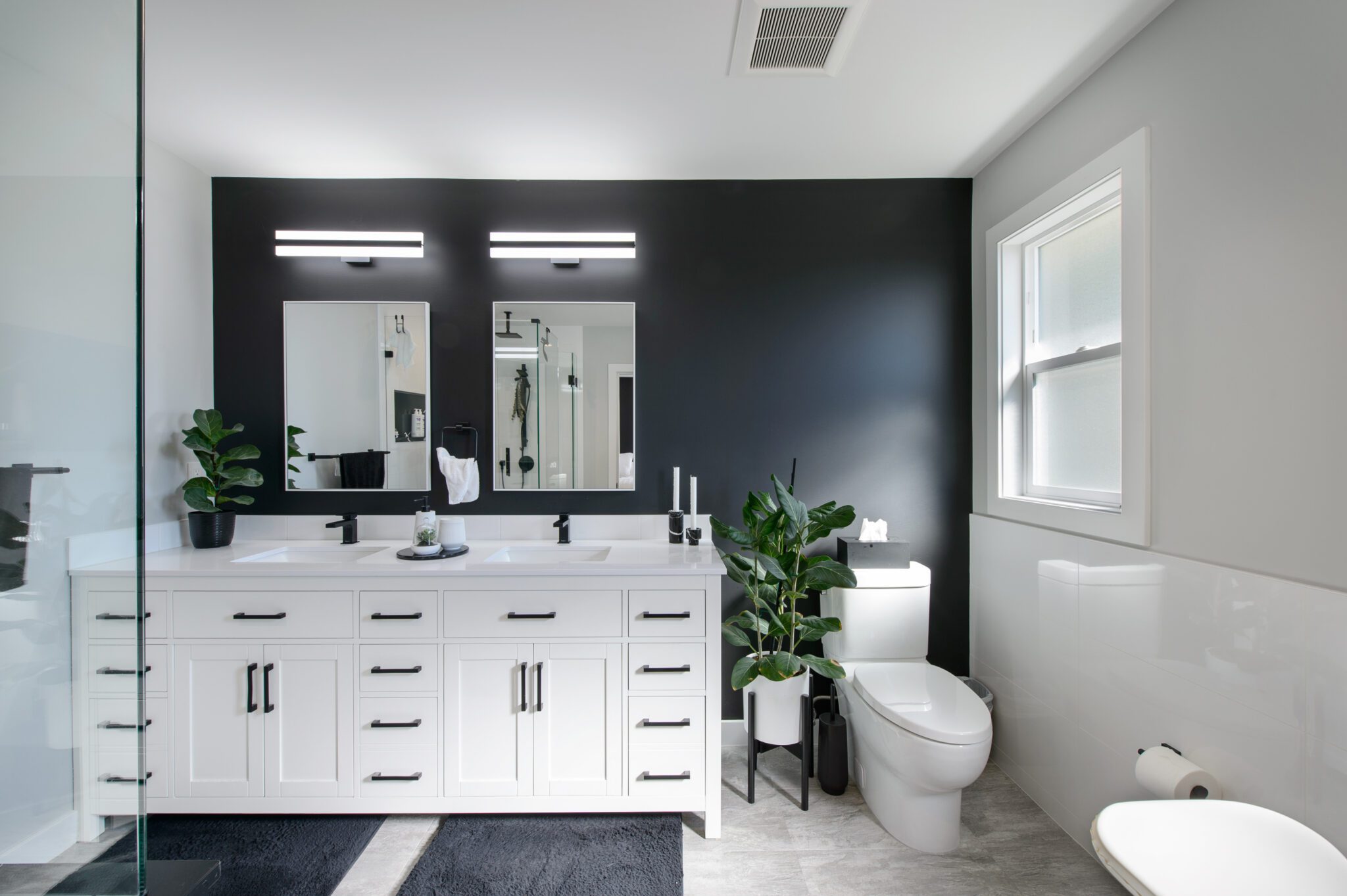 Bathroom with black accent wall, with a white double vanity and toilet.