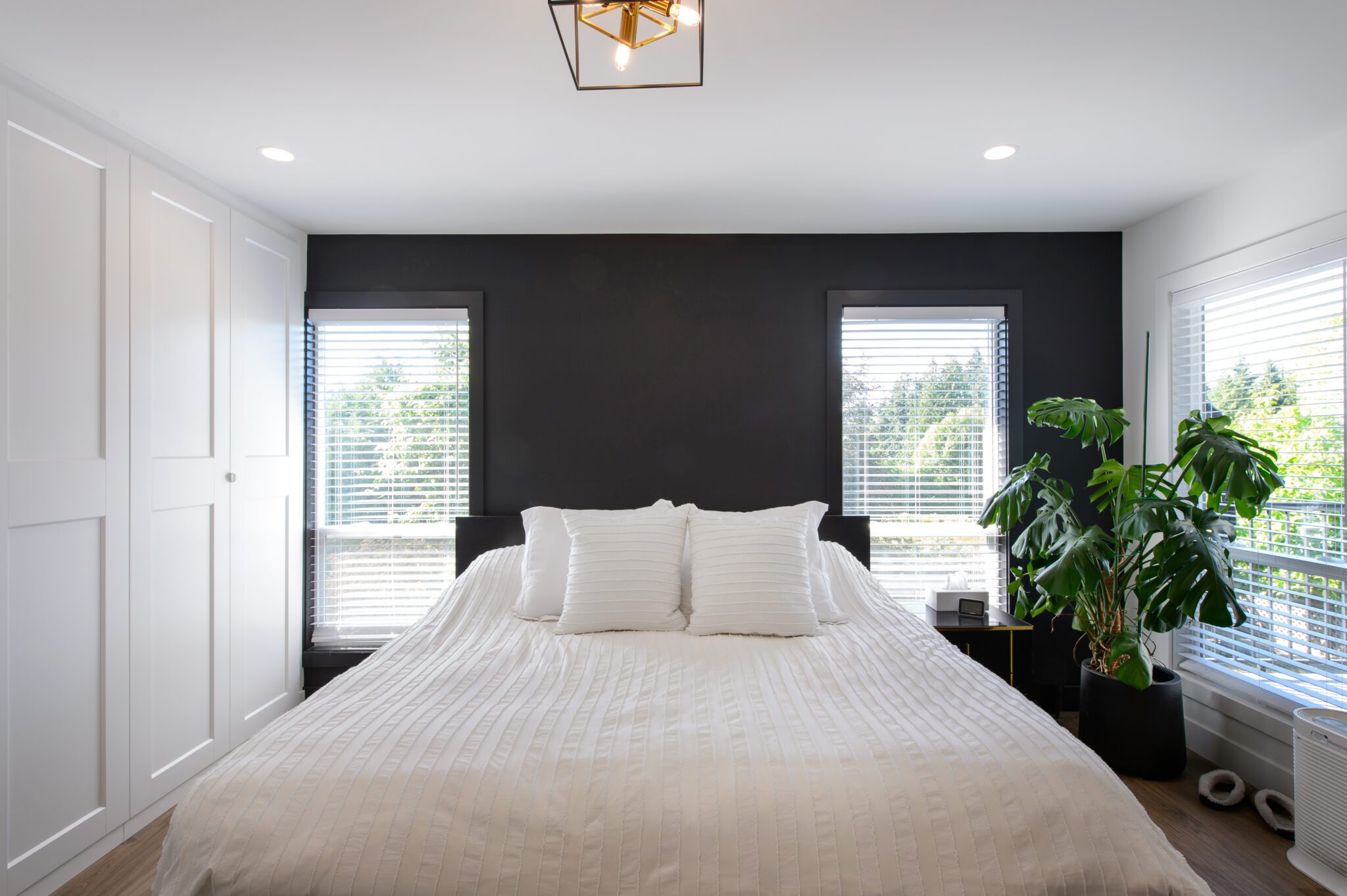 White bed nestled against a black wall, between two windows