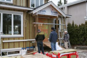 Three men standing in front of and facing an unfinished home.